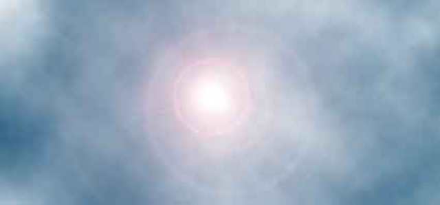 Immagine del sole (Per leggerne la descrizione proseguire nel link). Al centro il disco solare, abbagliante, in un cielo azzurro. Attorno al sole un effetto di foschia dovuto alla forte fonte di luce dell'astro.