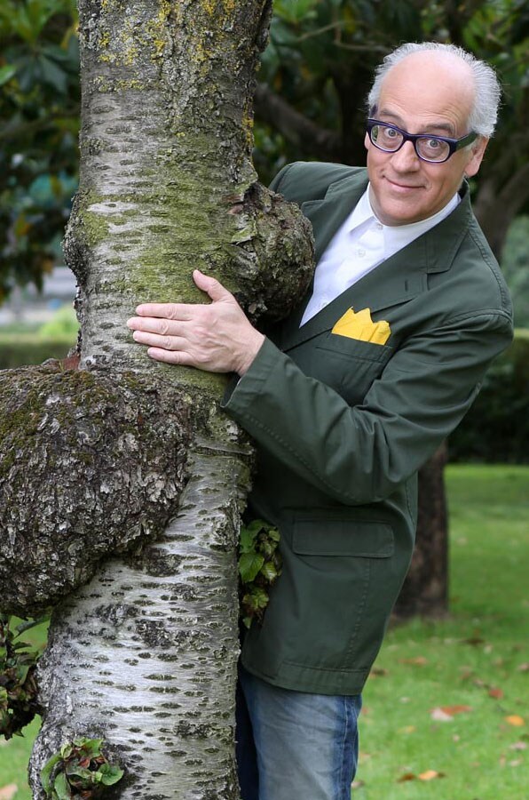 Piano americano di Guido Barlozzetti con giacca verde, da cui spunta una pochette gialla, mentre abbraccia un albero.