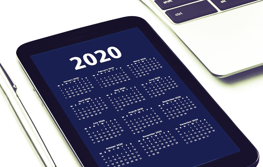 Tablet sul cui schermo di visualizza un calendario del 2020. Accanto si intravede parzialmente la tastiera di un computer portatile.