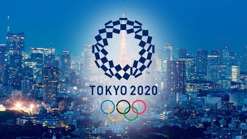 Sullo skyline notturno di Tokyo, il logo circolare di "Tokyo 2020" e al di sotto i cinque anelli olimpici.