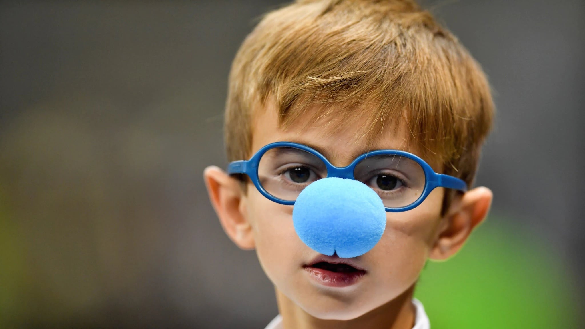 Un bambino di circa 6 anni con occhiali blu e una naso da pagliaccio azzurro.